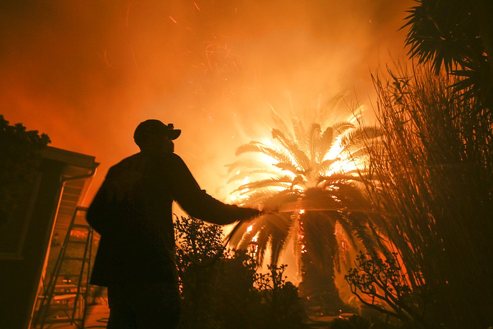 Park Billow, 27, sprays water on the hot spots in his backyard as the Woolsey Fire burns in Malibu, Calif., Friday, Nov. 9, 2018. Authorities announced Friday that a quarter of a million people are under evacuation orders as wind-whipped flames rage through scenic areas west of Los Angeles and burn toward the sea. (AP Photo/Ringo H.W. Chiu)