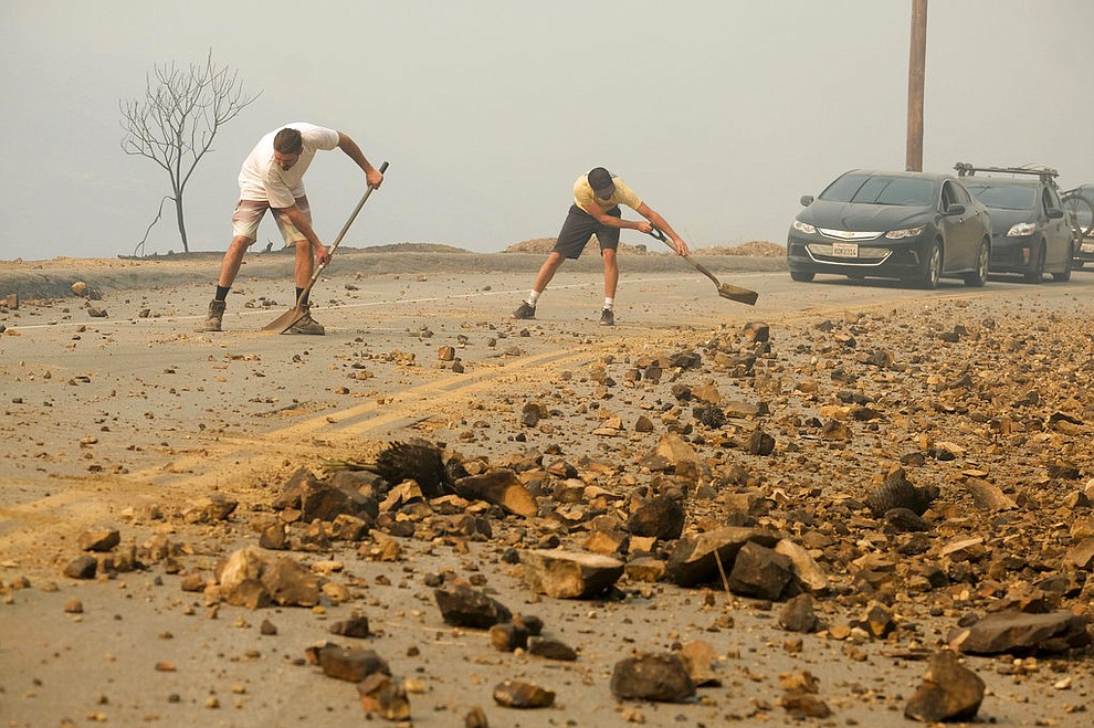Residents Damon Webb, left, and Brendon O'neal clean up the road after the Woolsey fire burned in Malibu, Calif., Saturday, Nov. 10, 2018.   Officials took advantage of temporarily calm conditions Saturday to assess damage from the blaze that's burned 109 square miles outside downtown Los Angeles. (AP Photo/Ringo H.W. Chiu)