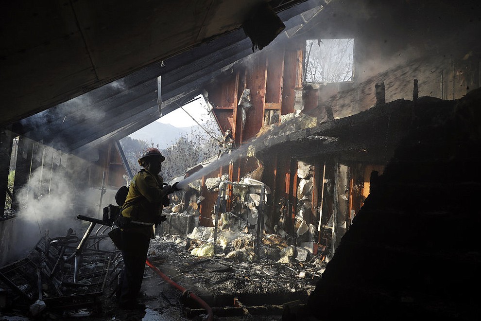 Capt. Adrian Murrieta with the Los Angeles County Fire Dept., hoses down hot spots on a wildfire-ravaged home Saturday, Nov. 10, 2018, in Malibu, Calif. Scores of houses from ranch homes to celebrities' mansions burned in a pair of wildfires that stretched across more than 100 square miles of Southern California, authorities said Saturday. (AP Photo/Marcio Jose Sanchez)