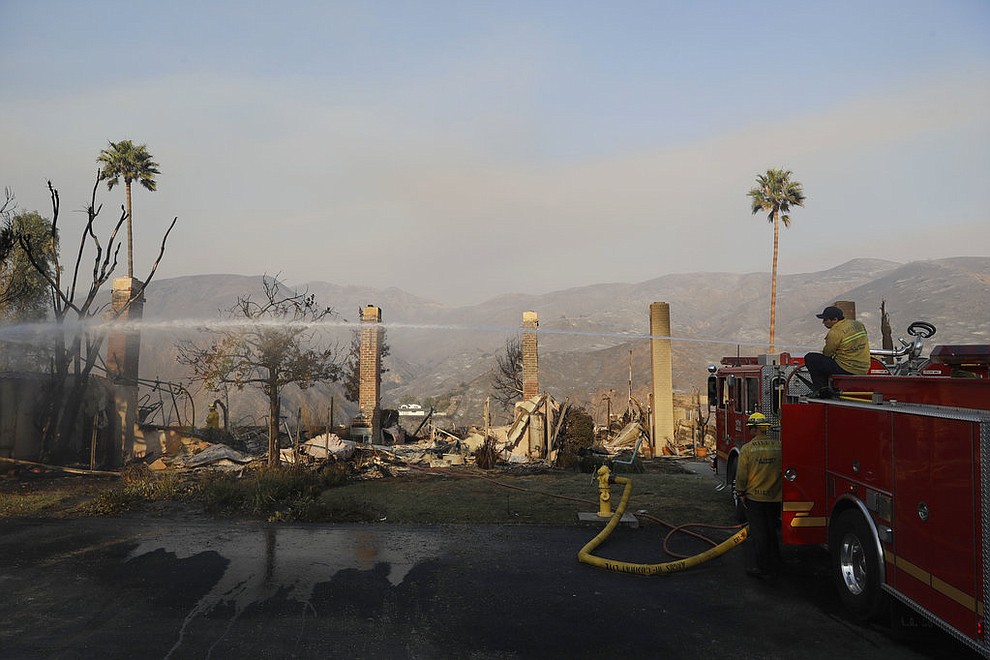 Firefighters hose down hot spots on a wildfire-ravaged property Saturday, Nov. 10, 2018, in Malibu, Calif. Scores of houses from ranch homes to celebrities' mansions burned in a pair of wildfires that stretched across more than 100 square miles of Southern California, authorities said Saturday. (AP Photo/Marcio Jose Sanchez)