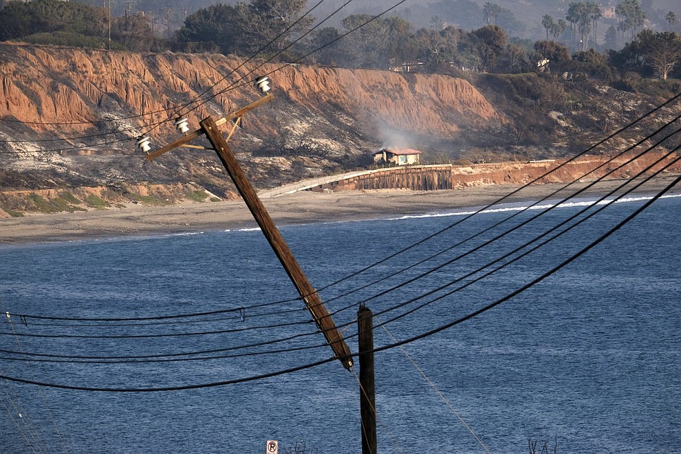 A smoldering hillside is seen in the distance behind a broken and burned telephone pole hanging along the Pacific Coast Highway outside of Malibu, Calif. on Saturday Nov. 10, 2018. (AP Photo/Richard Vogel)