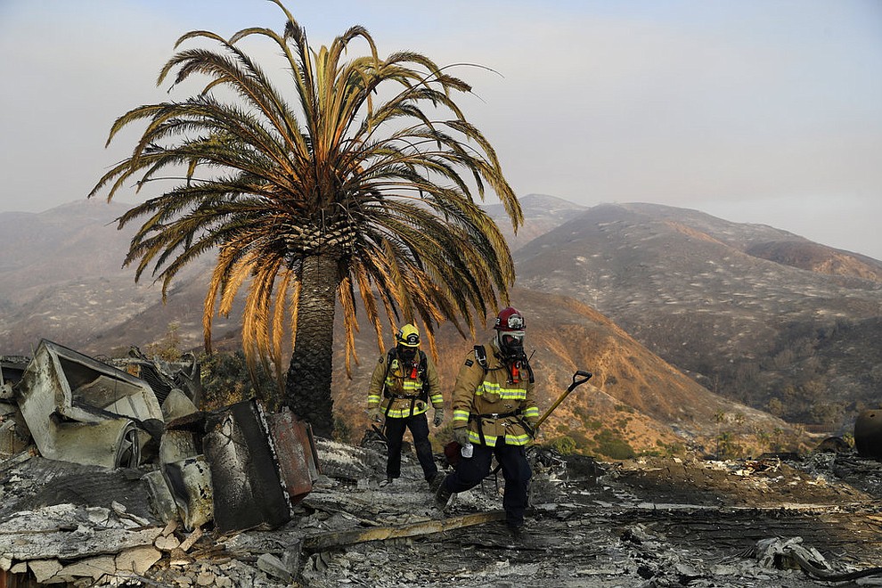 Firefighters Jason Toole, right, and Brent McGill with the Santa Barbara Fire Dept. walk among the ashes of a wildfire-ravaged home after turning off an open gas line on the property Saturday, Nov. 10, 2018, in Malibu, Calif. (AP Photo/Marcio Jose Sanchez)