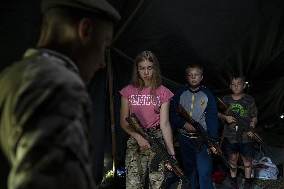 In this July 28, 2018 photo, participants of the "Temper of will" summer camp, organized by the nationalist Svoboda party, hold their AK-47 riffles as they receive instructions during a tactical exercise in a village near Ternopil, Ukraine. Campers as young as 8 years old practice using assault rifles. They are taught to shoot to kill Russians and their sympathizers. (AP Photo/Felipe Dana)