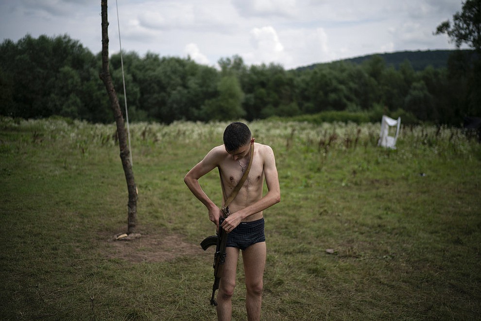 In this July 29, 2018 photo, Mykhailo adjusts his AK-47 riffle after bathing in a river during the "Temper of will" summer camp, organized by the nationalist Svoboda party, in a village near Ternopil, Ukraine. At 18, he is the oldest of the campers. "Every moment things can go wrong in our country. And one has to be ready for it," he said. "That's why I came to this camp. To study how to protect myself and my loved ones." (AP Photo/Felipe Dana)