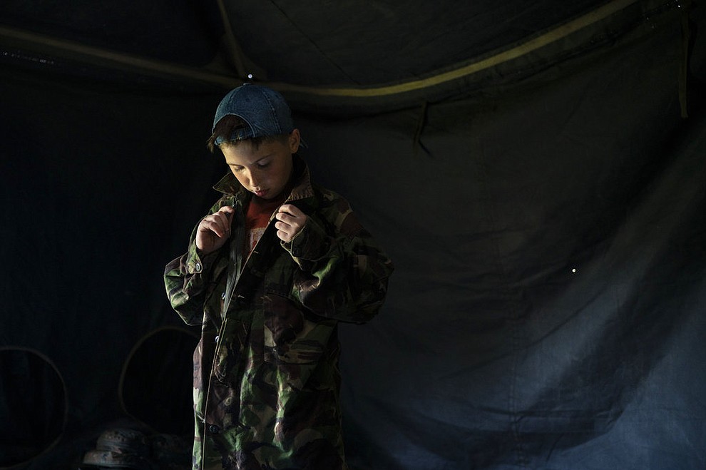 In this July 27, 2018 photo, a young participant of the "Temper of will" summer camp, organized by the nationalist Svoboda party, buttons up a camouflage shirt as he prepares for an exercise in a village near Ternopil, Ukraine. Campers as young as 8 years old practice using assault rifles. They are taught to shoot to kill Russians and their sympathizers. (AP Photo/Felipe Dana)