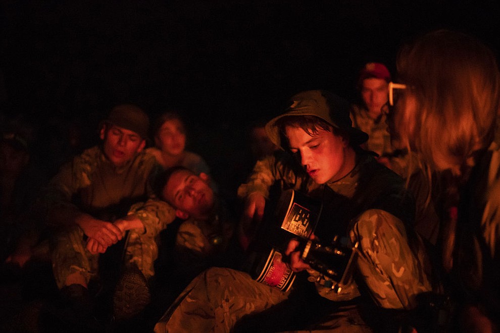 In this July 28, 2018 photo, a young participant of the "Temper of will" summer camp, organized by the nationalist Svoboda party, plays a guitar decorated with a sticker depicting bombs hitting a mosque, as others sing around a bonfire in a village near Ternopil, Ukraine. (AP Photo/Felipe Dana)
