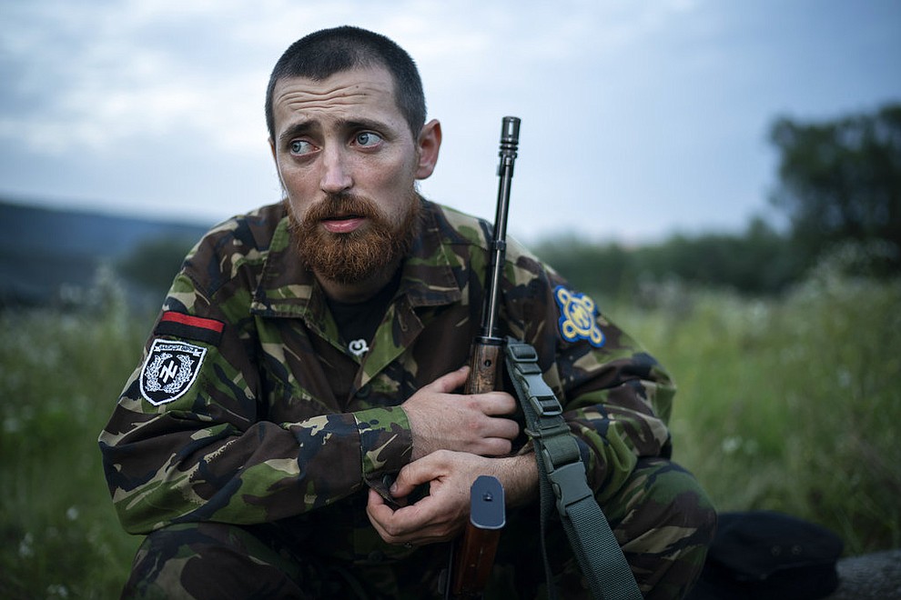 In this July 29, 2018 photo, Yuri "Chornota" Cherkashin, head of Sokil (Falcon), the youth wing of the nationalist Svoboda party, sits with his AK-47 rifle at the "Temper of will" summer camp in a village near Ternopil, Ukraine. "We never aim guns at people," he tells his campers. "But we don't count separatists, little green men, occupiers from Moscow as people, so we can and should aim at them." (AP Photo/Felipe Dana)