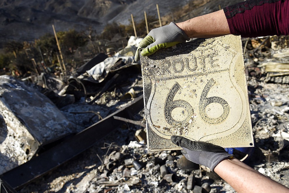 Donna Phillips shows a charred Route 66 sign she found among the possessions of her friend Marsha Maus, Sunday, Nov. 11, 2018, after wildfires tore through the Seminole Springs Mobile Home Park in Agoura Hills, Calif. Maus has been a resident of the neighborhood for 15 years. (AP Photo/Chris Pizzello)