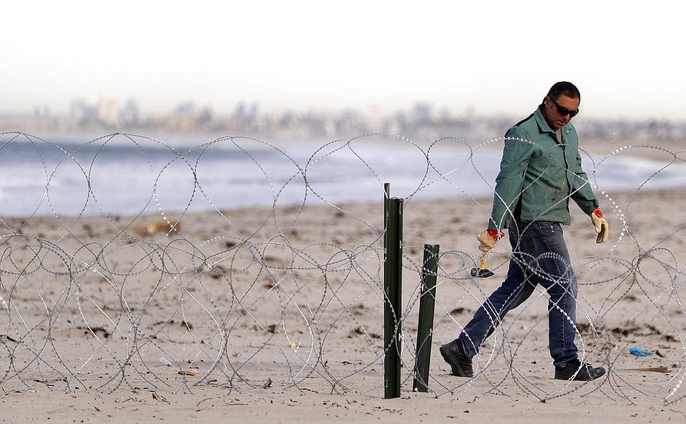 A worker installs concertina wire along the beach closest to the border, as the city of San Diego sits in the distance, as seen from Tijuana, Mexico, Wednesday, Nov. 14, 2018. Migrants in a caravan of Central Americans scrambled to reach the U.S. border, catching rides on buses and trucks for hundreds of miles in the last leg of their journey Wednesday as the first sizable groups began arriving in the border city of Tijuana. (AP Photo/Gregory Bull)