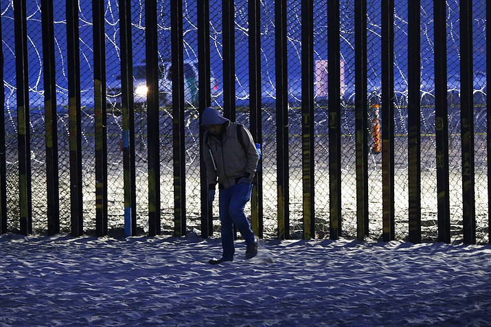 A resident walks near barriers, wrapped in concertina wire, separating Mexico and the United States, where the border meets the Pacific Ocean, in Tijuana, Mexico, Saturday, Nov. 17, 2018. Many of the nearly 3,000 migrants have reached the border with California. The mayor has called the migrants' arrival an "avalanche" that the city is ill-prepared to handle. (AP Photo/Marco Ugarte)