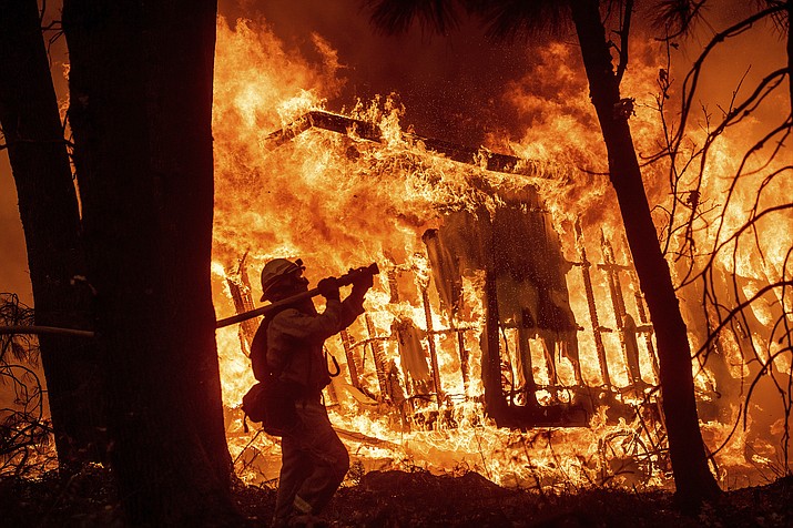 In this Nov. 9, 2018 file photo, firefighter Jose Corona sprays water as flames from the Camp Fire consume a home in Magalia, Calif. A massive new federal report warns that extreme weather disasters, like California’s wildfires and 2018’s hurricanes, are worsening in the United States. The White House report quietly issued Friday, Nov. 23 also frequently contradicts President Donald Trump. (Noah Berger/AP, File)