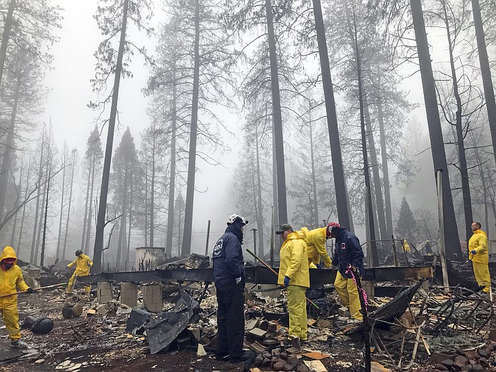 After a brief delay to let a downpour pass, volunteers resume their search for human remains at a mobile home park in Paradise, Calif., Friday, Nov. 23, 2018. A team from Orange County in Southern California is among several teams conducting a second search of a mobile home park after the deadly Camp wildfire torched part of Butte County in Northern California. Task force leader Craig Covey, in blue jacket at center, says his team is doing a second search because there are outstanding reports of missing people whose last known address was at the mobile home park. (AP Photo/Kathleen Ronayne)