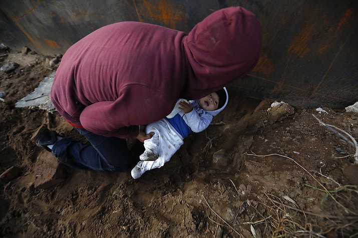 Honduran migrant Joel Mendez, 22, passes his eight-month-old son Daniel through a hole under the U.S. border wall to his partner, Yesenia Martinez, 24, who had already crossed in Tijuana, Mexico, Friday, Dec. 7, 2018. Moments later Martinez surrendered to waiting border guards while Mendez stayed behind in Tijuana to work, saying he feared he'd be deported if he crossed. (AP Photo/Rebecca Blackwell)
