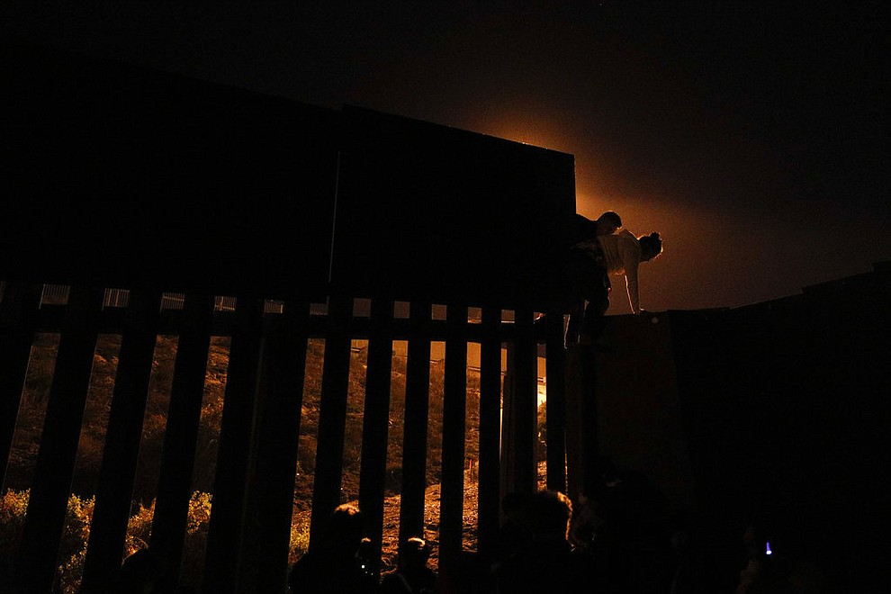 In a photo taken from Playas of Tijuana, Mexico, Honduran migrants climb over a section of the U.S. border fence before handing themselves in to border control agents, Sunday, Dec. 2, 2018. A steady trickle of Central American migrants have been finding ways to climb over, tunnel under or slip through the U.S. border wall to plant their feet on U.S. soil and ask for asylum. (AP Photo/Rebecca Blackwell)