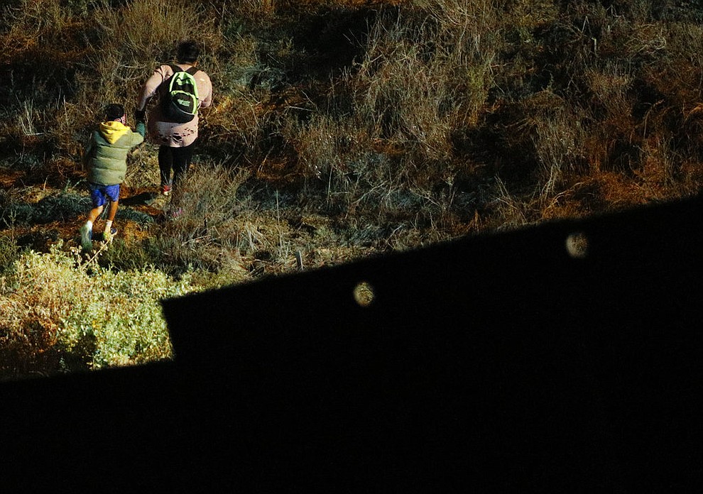 A woman and child migrant start up a hill in San Ysidro, California after climbing over the U.S. border wall from Playas de Tijuana, Mexico, where many migrants expecting to surrender to U.S. border guards were crossing, Monday, Dec. 3, 2018. Discouraged by long waits at ports of entry and sometimes fearing for their lives, migrants are loath to accept the alternative. (AP Photo/Rebecca Blackwell)
