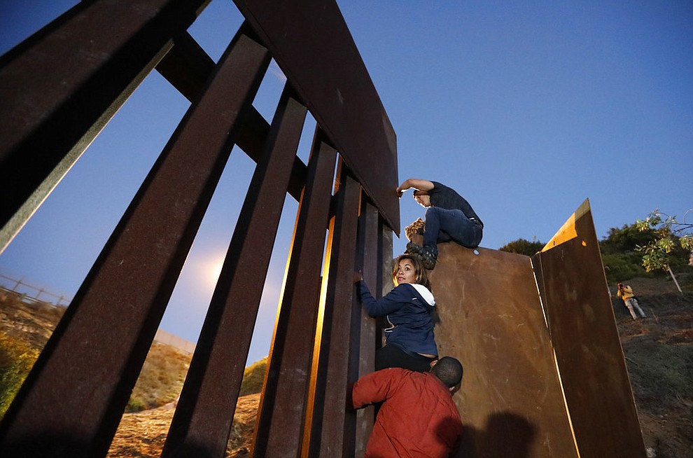 Central American migrants planning to surrender to U.S. border patrol agents climb over the U.S. border wall from Playas de Tijuana, Mexico, late Monday, Dec. 3, 2018. Thousands of migrants are living in crowded tent cities in the Mexican city of Tijuana after undertaking a grueling, weeks-long journey to the U.S. border. (AP Photo/Rebecca Blackwell)