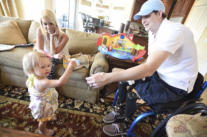 In this AprIl 1, 2015, file photo, retired Air Force Airman Brian Kolfage, right, gives a piece of cheese to his 1-year-old daughter Paris, as his wife Ashley looks on at their recently rented home in Sandestin, Fla. Kolfage, a triple-amputee who lost his limbs serving in Iraq in the U.S. Air Force, started a GoFundMe page to help pay for construction of President Donald Trump’s border wall that has already raised millions of dollars. (Nick Tomecek/Northwest Florida Daily News via AP, file)
