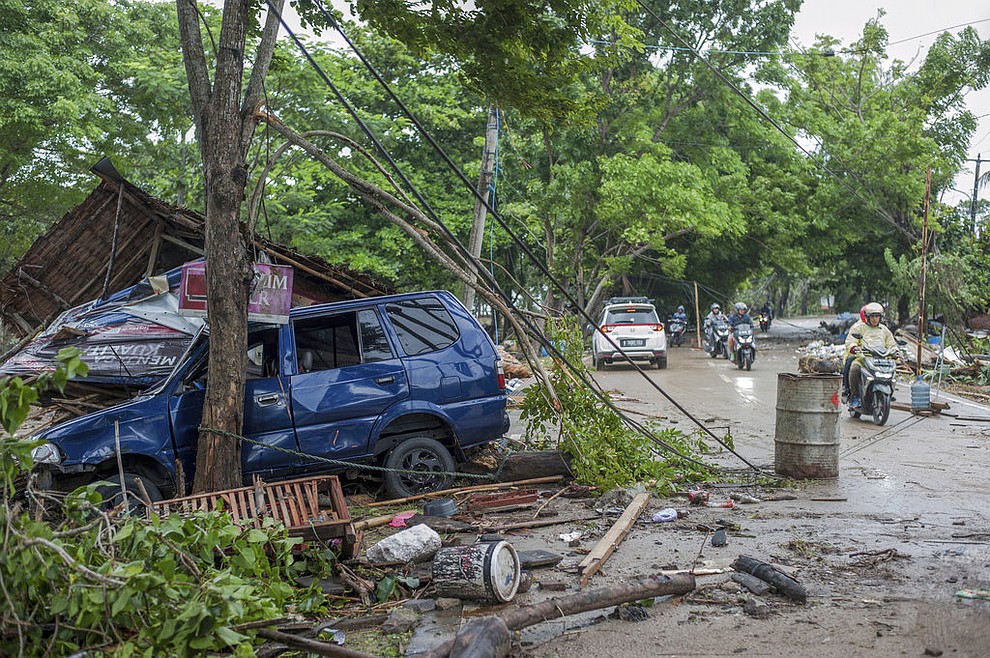 Motorists pass by a car swept away by a tsunami in Carita, Indonesia, Sunday, Dec. 23, 2018. The tsunami occurred after the eruption of a volcano around Indonesia's Sunda Strait during a busy holiday weekend, sending water crashing ashore and sweeping away hotels, hundreds of houses and people attending a beach concert. (AP Photo/Fauzy Chaniago)
