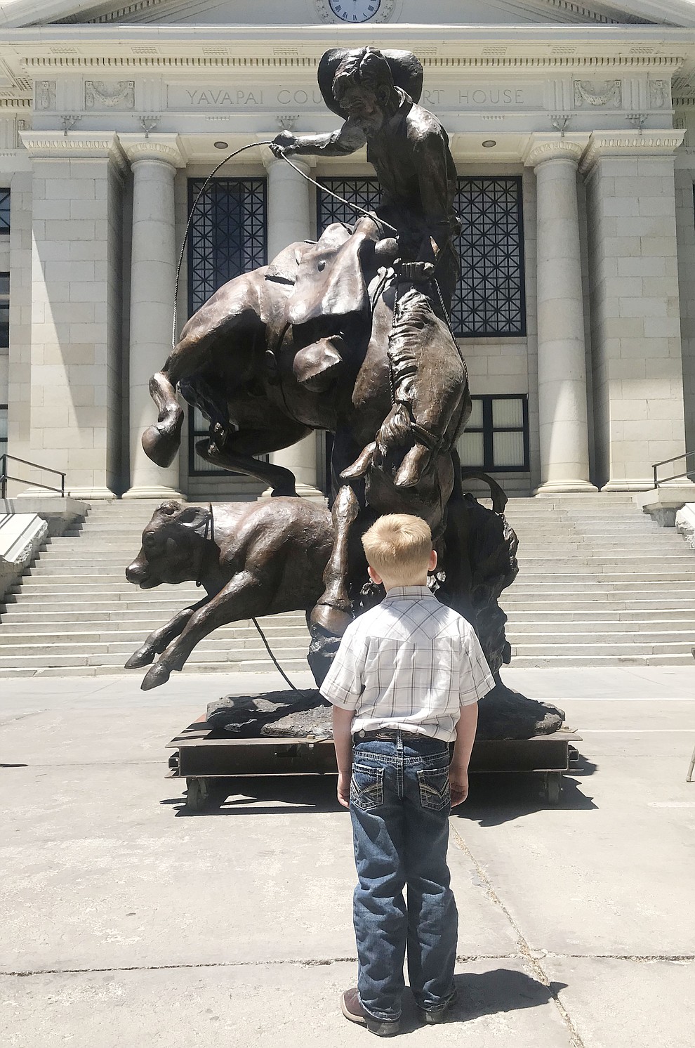 Five-year old Sterling Beach looks up at the statue called Cowboy in a Storm at the 44th Annual Phippen Museum Western Art Show on the courthouse plaza Saturday, May 26, 2018 in downtown Prescott. The statue eventually will be placed in the middle of the roundabout on Highway 89 in front of the Phippen Museum. Beach's father Christian worked on the statue at Bronzesmith in Prescott Valley. (Les Stukenberg/Courier)