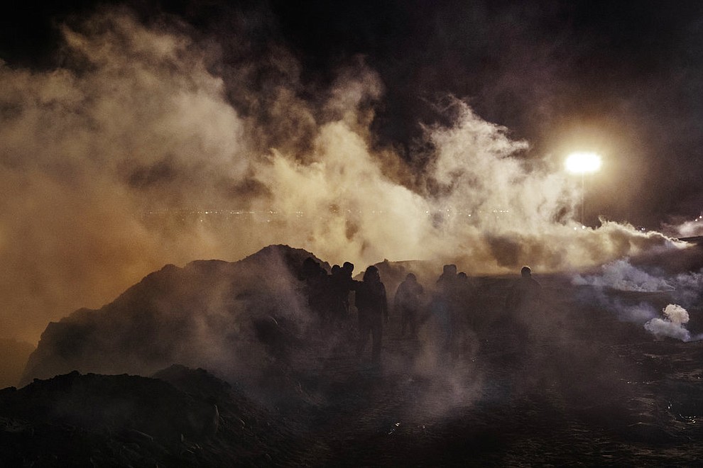 Migrants run as tear gas is thrown by U.S. Border Protection officers to the Mexican side of the border fence after they climbed the fence to get to San Diego, Calif., from Tijuana, Mexico, Tuesday, Jan. 1, 2019. Discouraged by the long wait to apply for asylum through official ports of entry, many migrants from recent caravans are choosing to cross the U.S. border wall and hand themselves in to border patrol agents. (AP Photo/Daniel Ochoa de Olza)