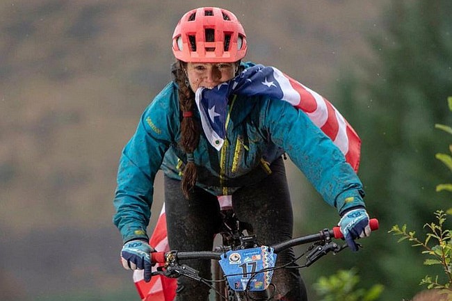 Mountain biker Kaitlyn Boyle of Prescott clenches an American flag with her teeth en route to winning the Solo 24-Hour World Championships in Fort William, Scotland, in October 2018. Boyle is recovering from a serious car accident that occurred Dec. 24, 2018, in Idaho. (Courtesy/visitnewengland.com.au)