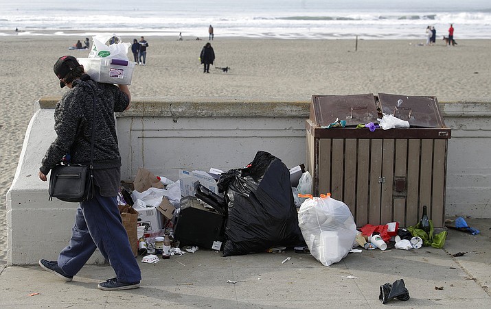 A woman walks past trash piled next to a garbage bin at Ocean Beach in San Francisco, Thursday, Jan. 3, 2019. Nonprofits, businesses and state governments across the country are paying bills and putting in volunteer hours in an uphill battle to keep national parks safe and clean for visitors as the partial U.S. government shutdown lingers. (AP Photo/Jeff Chiu)