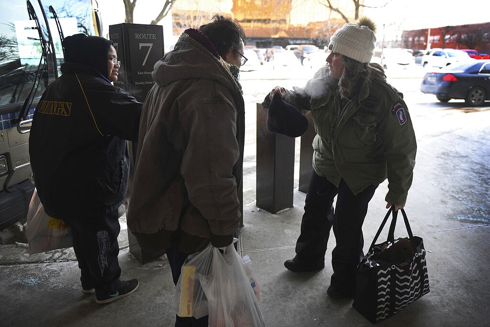 Amy Lawrence, right, helps someone wear a hat as she walks around the downtown bus stop terminal, handing out hand warmers to passengers in Sioux Falls, S.D., Tuesday, Jan. 29, 2019. Temperatures in the Dakotas and Minnesota dropped on Tuesday to as low as minus 27 (negative 33 degrees Celsius) with wind chills as cold as minus 59 (negative 51 degrees Celsius). (Briana Sanchez/The Argus Leader via AP)