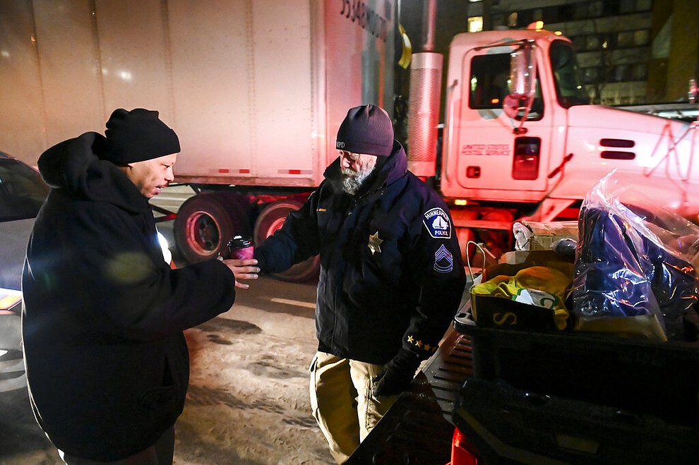 Minneapolis Police Sgt. Grant Snyder, right, hands a cup of hot chocolate to Dawone Boclair outside the public library on Hennepin Avenue in downtown Minneapolis, as the temperatures dipped well below freezing, Tuesday, Jan. 29, 2019. Snyder will be hitting the streets Tuesday and Wednesday night during the height of the big chill to check on the welfare of homeless people who haven't made it into a shelter. (Aaron Lavinsky/Star Tribune via AP)