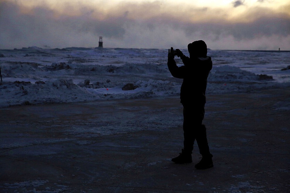 A man takes pictures as ice forms along the shore of Lake Michigan, Wednesday, Jan. 30, 2019, in Chicago. A deadly arctic deep freeze enveloped the Midwest with record-breaking temperatures on Wednesday, triggering widespread closures of schools and businesses, and prompting the U.S. Postal Service to take the rare step of suspending mail delivery to a wide swath of the region. (AP Photo/Kiichiro Sato)