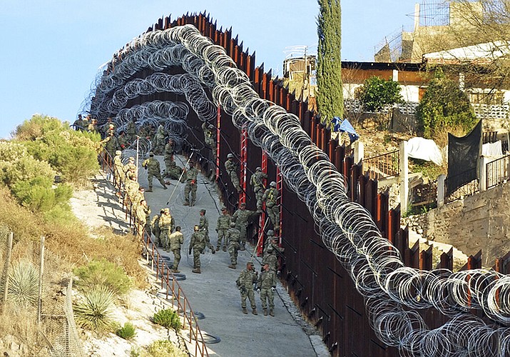In this Saturday, Feb. 2, 2019 photo, U.S. Army troops place additional concertina wire to the border fence on a hillside above Nelson Street in downtown Nogales, Ariz. Nogales, Mexico is seen at right. The small Arizona border city is fighting back against the installation of razor fencing that now covers the entirety of a tall border fence along the city's downtown area. (Jonathan Clark/Nogales International via AP)