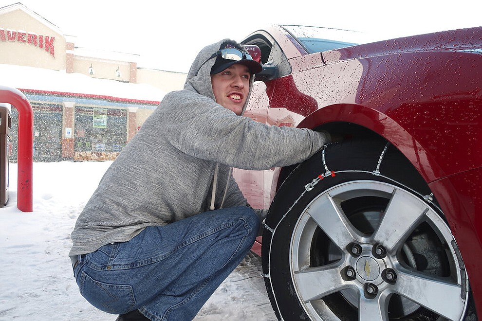 Taylor Killian puts snow chains on the vehicle he's driving during a trip to Flagstaff, Arizona, on Thursday, Feb. 21, 2019. Schools across northern Arizona canceled classes and some government offices decided to close amid a winter storm that's expected to dump heavy snow in the region. (AP Photo/Felicia Fonseca)