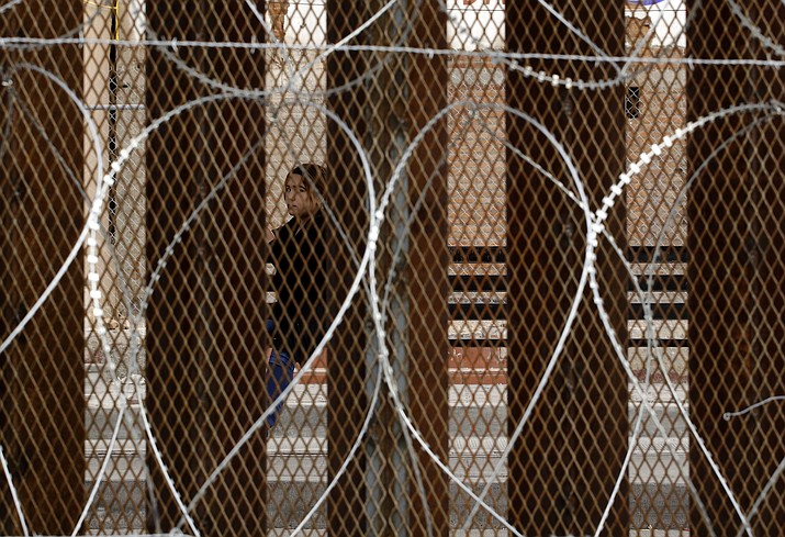 A woman waiting for a bus in Nogales, Mexico, is framed by a razor-wire-covered border wall separating it from Nogales, Ariz., Saturday, March 2, 2019. (Charlie Riedel/AP)