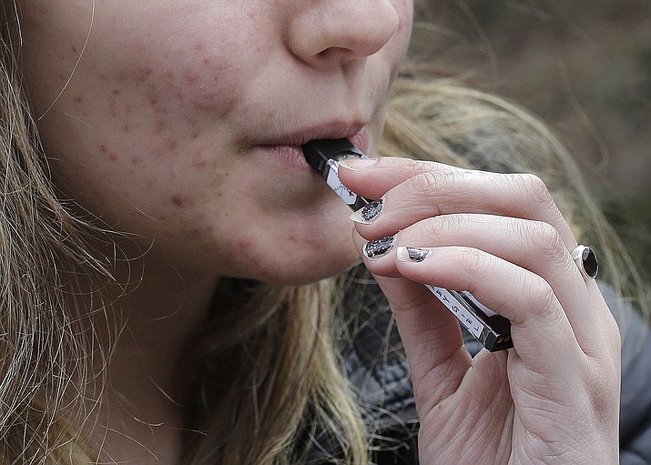 In this April 11, 2018, file photo, a high school student uses a vaping device near a school campus in Cambridge, Mass. U.S. health regulators are moving ahead with a plan to keep e-cigarettes out of the hands of teenagers by restricting sales of most flavored products in convenience stores and online. (Steven Senne/AP, File)