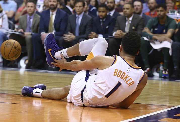 An injured Phoenix Suns guard Devin Booker reaches for his ankle after turning it during the first half of the team's NBA basketball against the Utah Jazz on Wednesday, April 3, 2019, in Phoenix. (Ross D. Franklin/AP)