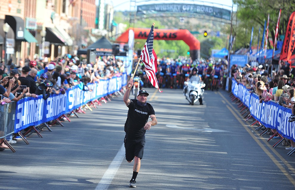 Kaolin Cummens runs the American flag up Whiskey Row before the Whiskey Off Road Pro 50-mile cross country mountain bike race in Prescott Sunday, April 28. (Les Stukenberg/Courier)
