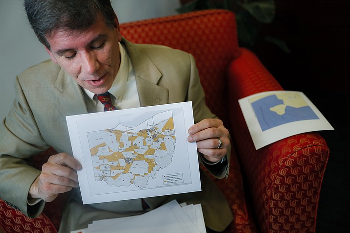 In this April 11, 2019 file photo, David Niven, a professor of political science at the University of Cincinnati holds a map displaying the wide disparity of Ohio congressional district office locations, with orange locations representing areas whose office are found outside it's own district's bounds, in Cincinnati. A federal court ruled Friday, May 3 that Ohio's congressional map is unconstitutional and ordered a new one be drawn for the 2020 elections. (John Minchillo/AP, file)