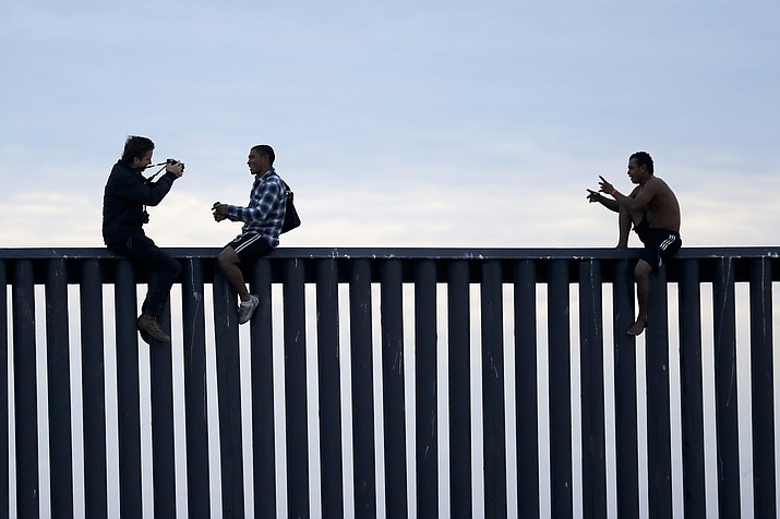 In this Nov. 21, 2018, file photo, two Honduran men pose as a photographer, at left, takes their picture after the group climbed the border wall separating Tijuana, Mexico, and San Diego, before climbing back down on the Mexican side, seen from San Diego. (Gregory Bull/AP, File)