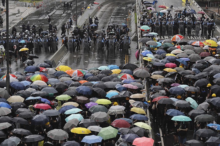 Protesters holding umbrellas face off police officers in anti-riot gear in Hong Kong on Monday, July 1, 2019. Protesters in Hong Kong pushed barriers and dumpsters into the streets early Monday morning in an apparent bid to block access to a symbolically important ceremony marking the anniversary of the return of the former British colony to China. (AP Photo/Kin Cheung)