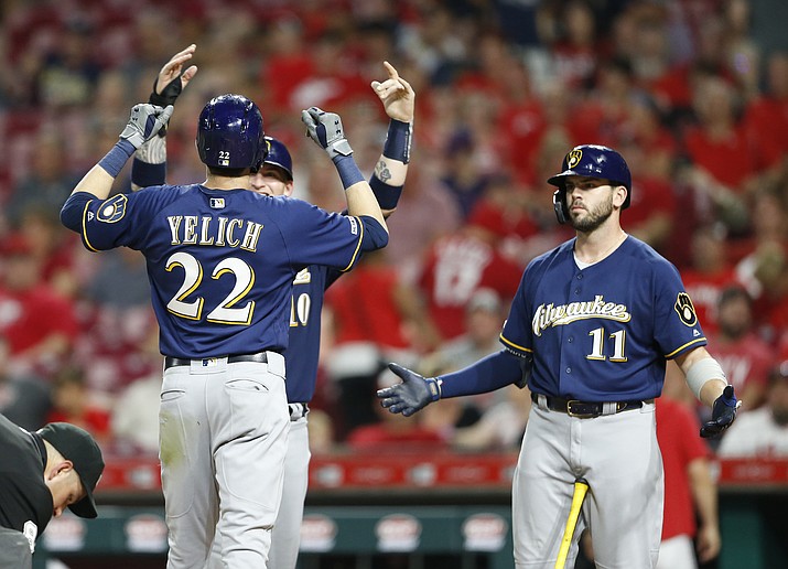 Milwaukee Brewers' Christian Yelich (22) is congratulated at the plate by Yasmani Grandal, obscured, left, and Mike Moustakas (11) following a two-run home run off Cincinnati Reds relief pitcher Robert Stephenson during the ninth inning of a baseball game, Monday, July 1, 2019, in Cincinnati. (Gary Landers/AP)