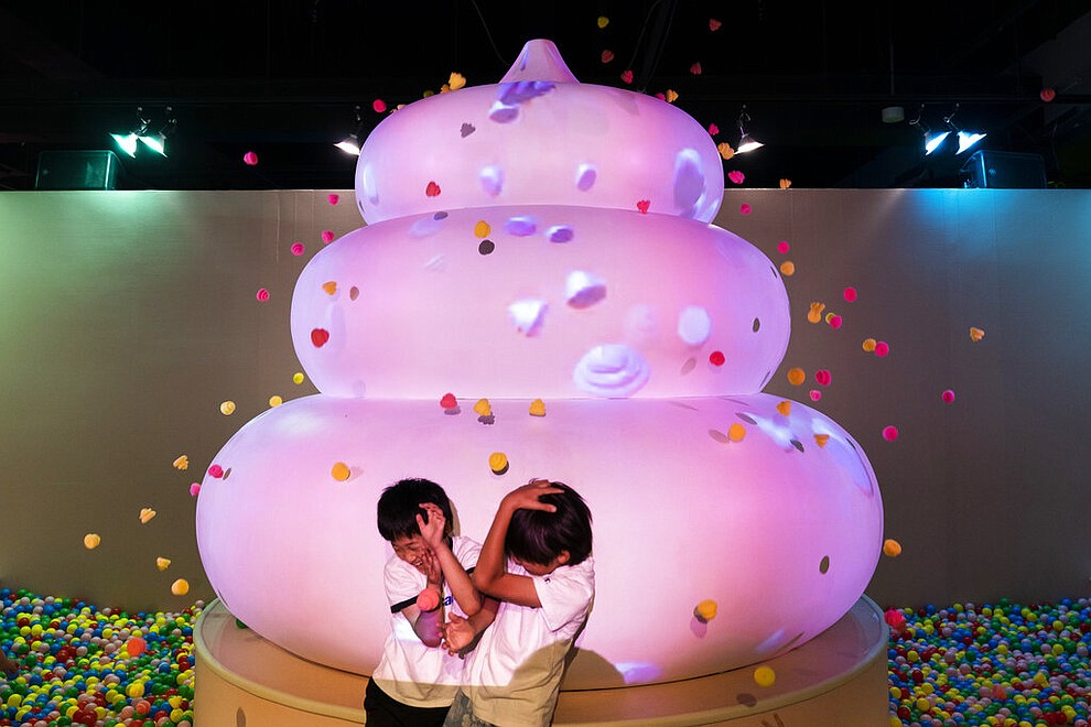In this Tuesday, June 18, 2019, photo, two boys jokingly take cover as small toy poops gush from a giant poop-shaped inflatable at the Unko Museum in Yokohama, south of Tokyo. In a country known for its cult of cute, even poop is not an exception. A pop-up exhibition at the Unko Museum in the port city of Yokohama is all about unko, a Japanese word for poop. The poop installations there get their cutest makeovers. They come in the shape of soft cream, or cupcake toppings. (AP Photo/Jae C. Hong)