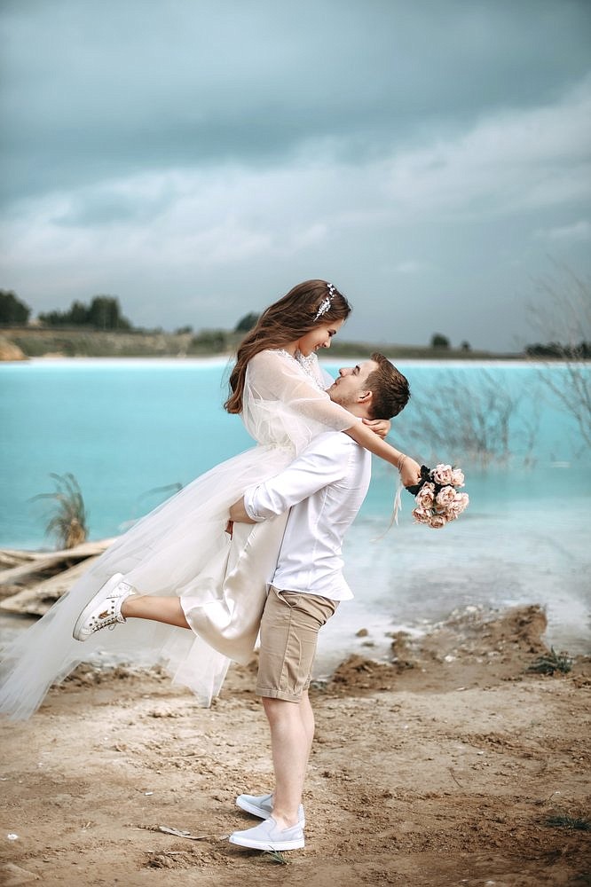 In this handout photo taken by ekaterinaaaaks on Sunday, June 23, 2019, a newlywed couple pose for a photo by a lake and a power station in the background are seen in the Siberian city of Novosibirsk, about 2,800 kilometers (1,750 miles) east of Moscow, Russia. (ekaterinaaaaks via AP)