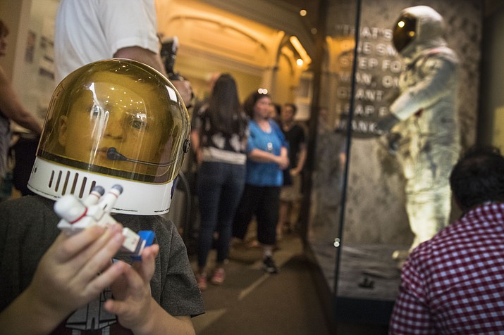 Jack Heely, 5, of Alexandria, Va., wears a toy space helmet as he arrives as one of the first visitors to view Neil Armstrong's Apollo 11 spacesuit, background, after it is unveiled at the Smithsonian's National Air and Space Museum on the National Mall in Washington, Tuesday, July 16, 2019. (AP Photo/Andrew Harnik)