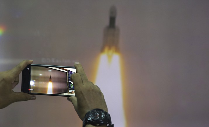 A man at New Delhi's Nehru Planetarium, takes pictures of a web cast of the lift off of Indian Space Research Organization (ISRO)'s Geosynchronous Satellite launch Vehicle (GSLV) MkIII carrying Chandrayaan-2 from Satish Dhawan Space center in Sriharikota, India, Monday, July 22, 2019. India's space agency says it has launched an unmanned spacecraft to the far side of the moon a week after aborting the mission due to a technical problem. (AP Photo/Manish Swarup)