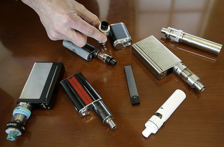 In this Tuesday, April 10, 2018 photo, a high school principal displays vaping devices that were confiscated from students at the school in Massachusetts. On Wednesday, Aug. 14, 2019, the Vapor Technology Association filed a lawsuit against the U.S. government to delay a review of electronic cigarettes. (AP Photo/Steven Senne)