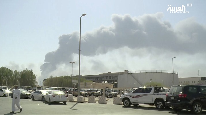 In this image made from a video broadcast on the Saudi-owned Al-Arabiya satellite news channel on Saturday, Sept. 14, 2019, a man walks through a parking lot as the smoke from a fire at the Abqaiq oil processing facility can be seen behind him in Buqyaq, Saudi Arabia. (Al-Arabiya via AP)