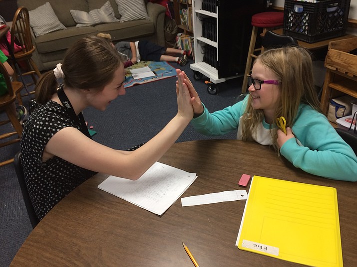Prescott High School senior Katie Kwiatowski gets a high-five from Taylor Hicks Elementary third-grader Ellie Peterson as they work together on a writing assignment in Kathy Bishop’s class. Katie is one of four high school students participating in a pilot project as AmeriCorps State and National members assigned to work with students in area classrooms. Prescott High and Northpoint Expeditionary Learning Academy are the first two high schools to participate. (Nanci Hutson/Courier)