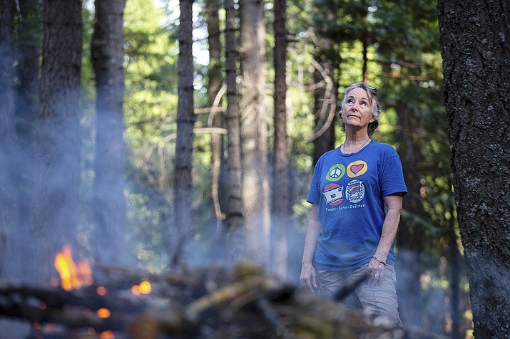 In this photo taken June 13, 2019, Kelly Loew is creating defensible space around her home in Shingletown, Calif., by trimming pine branches and burning them in a pile. (Anton L. Delgado/News21 via AP)