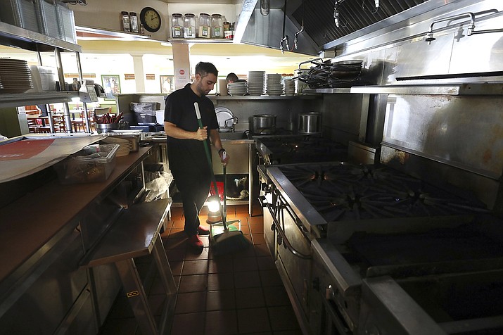 Salvador Espinosa sweeps in the kitchen of a Mary's Pizza Shack restaurant during a Pacific Gas and Electric Co. power shutdown in Santa Rosa, Calif., Thursday, Oct. 10, 2019. More than 1.5 million people in Northern California were in the dark Thursday, most for a second day, after the state's biggest utility shut off electricity to many areas to prevent its equipment from sparking wildfires as strong winds sweep through the region. (Christopher Chung/The Press Democrat via AP)