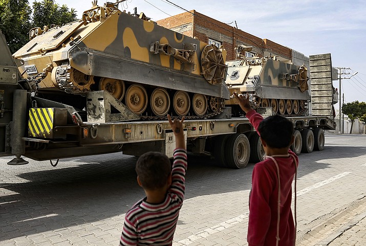 Children wave to a Turkish forces truck transporting armoured personnel carriers at the border with Syria in Karkamis, Gaziantep province, southeastern Turkey, Tuesday, Oct. 15, 2019. Turkey defied growing condemnation from its NATO allies to press ahead with its invasion of northern Syria on Tuesday, shelling suspected Kurdish positions near the border amid reports that Syrian Kurds had retaken a key town. (Emrah Gurel/AP)