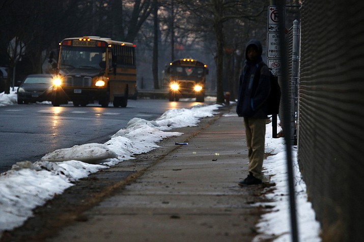 In this Feb. 5, 2019, photo, a student waits for a bus outside the abandoned John C. Clark Elementary and Middle School in Hartford, Conn. The school was closed in 2015 after toxic PCBs were found during a renovation. Many students in the neighborhood now must travel long distances to get to other schools. (Martha Irvine/AP)